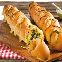 Zwei gefüllte Baguettes zum Grillen, eines mit Kräutern und Käse, das andere mit Pesto und Tomaten, daneben eine Schüssel Dip.