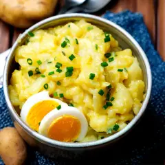 Schüssel mit warmem Kartoffelsalat, garniert mit Schnittlauch und Ei. Ein Klassiker, der immer schmeckt.