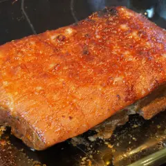 Saftiger Schweinebraten sous vide mit knuspriger Kruste, glänzend und goldbraun, ruht in einer Glasschale.