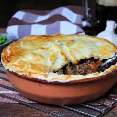 Herzhaftes Steak Pie mit goldbrauner Kruste, dane eine Schüssel Erbsen und ein Glas dunkles Bier.