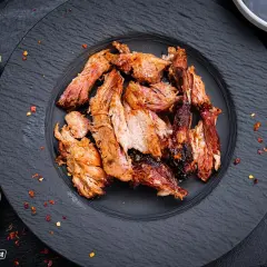 Zartes Pulled Pork auf schwarzem Teller, perfekt gegart. Die Kerntemperatur ist entscheidend für saftiges Fleisch. Ingwer und Knoblauch deuten auf würzige Aromen hin.