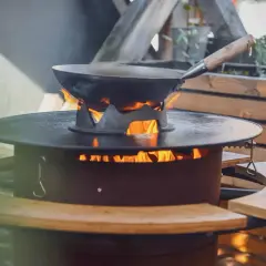 Ein Wok auf einem Feuerring, der an eine Plancha erinnert, wird draußen erhitzt.