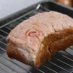 Ein Krustenbraten liegt auf einem Rost, bereit zum Krustenbraten grillen. Die Schwarte ist eingeschnitten und mit Gewürzen bestreut.