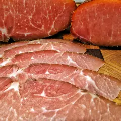 Dünn geschnittener Lachsschinken, der aus magerem Schweinefleisch besteht, liegt auf einem Holzbrett.