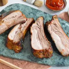 Saftige, dicke Rippe vom Grill, perfekt gegart, liegen auf einem grünen Marmorbrett. Dazu gibt es Ketchup und Senf.