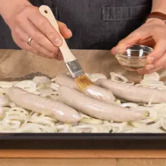 Bratwurst im Backofen: Mit einem Pinsel wird die Wurst mit Öl bestrichen, bevor sie auf Zwiebeln im Ofen gart.