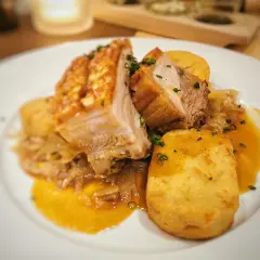 Saftiger Schweinebraten Niedrigtemperatur mit knuspriger Kruste, Kartoffelklößen und dunkler Soße auf einem weißen Teller.