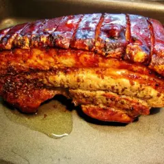 Perfekt gegrillter Schweinebauch mit knuspriger Schwarte liegt in einer Bratpfanne. Der Bratensaft glänzt daneben.