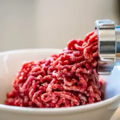 Frisches Hackfleisch wird aus einem Fleischwolf in eine Schüssel gedrückt. So kann man Hackfleisch selber machen.