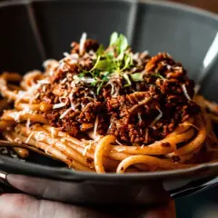Eine Schüssel mit köstlichen Spaghetti Bolognese, garniert mit frischen Kräutern und geriebenem Parmesan.