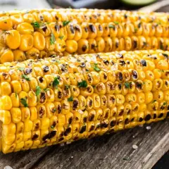 Zwei perfekt gegrillte Maiskolben mit gerösteten Stellen und Kräutern, bereit zum Genießen. Das Maiskolben grillen ist ein Sommergenuss.