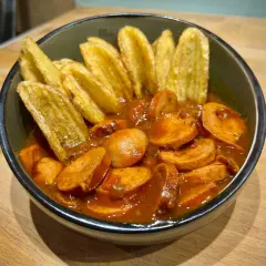 Eine Schüssel mit geschnittener Currywurst in Sauce und Kartoffelspalten. Perfekt für einen gemütlichen Abend, wie aus dem Dutch Oven.