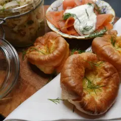 Goldbraune Yorkshire Pudding-Törtchen mit Dill garniert, daneben Lachs mit Frischkäse und ein Glas Sauerkraut.