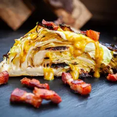 Ein Stück Spitzkohl, gegrillt und mit einem cremigen Senfdressing beträufelt, garniert mit knusprigen Speckwürfeln.