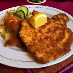 Perfekt paniertes Wiener Schnitzel mit Kartoffelsalat, Tomate, Gurke und Zitrone. Ein Genuss, der zeigt, wie gut Wiener Schnitzel panieren gelingt.