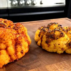 Zwei perfekt gegrillte Blumenkohlröschen liegen auf einem Holzbrett. Sie sind goldbraun und leicht angekohlt, was auf köstliches blumenkohl grillen hindeutet.