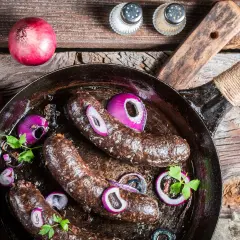 Bratwürste in der Pfanne mit Zwiebeln und Petersilie. Was ist Black Pudding? Eine herzhafte Wurstspezialität, die hier gebraten wird.