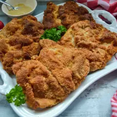 Goldbraun paniertes Schnitzel, perfekt zum Schnitzel panieren. Dazu Radieschen, Petersilie und Senf.