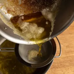 Braunes Butter wird durch ein Sieb gegossen, um die festen Bestandteile zu entfernen.