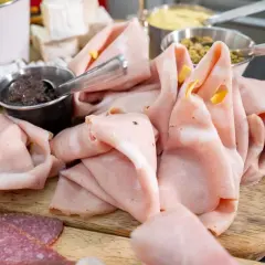 Dünn geschnittene Mortadella, eine italienische Brühwurst, liegt auf einem Holzbrett neben Salami und Oliven.