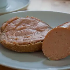 Ein Brötchen mit Teewurst und ein Stück Teewurst daneben. So sieht die beliebte Teewurst aus.