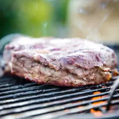 Ein saftiges Rindersteak grillen, Rauch steigt auf, die Flammen lodern darunter. Perfekt für den Grillabend!