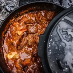 Herzhaftes Brauhaus Gulasch köchelt in einem gusseisernen Topf über glühender Asche. Ein Fest für die Sinne!