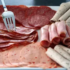 Eine Auswahl an Aufschnitt, darunter Salami und Schinken, liegt auf einer Platte. Eine Gabel steckt in den Scheiben, bereit zum Servieren oder zur Aufbewahrung.