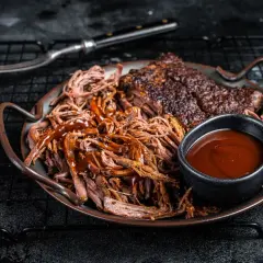 Saftiges pulled pork mit BBQ-Sauce und Beilagen auf einem Teller. Ein Gabel liegt daneben.