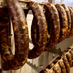 Reife, dunkle Würste hängen an einer Stange. Sie sehen aus wie eine traditionelle Chorizo, die zum Trocknen bereit ist.