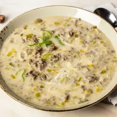 Eine cremige hackfleisch lauch suppe, garniert mit frischem Lauch und Gewürzen, serviert in einer rustikalen Schüssel.