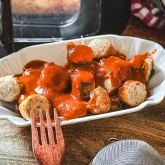 Leckere Currywurst im Airfryer, serviert mit einer würzigen Currysauce und einem Hauch Currypulver.