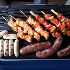 Fleisch auf Gasgrill richtig grillen: Hähnchenspieße und Würstchen brutzeln auf dem Grill.
