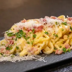 Ein Teller cremiger Spaghetti Carbonara, garniert mit Speckwürfeln, Petersilie und frisch geriebenem Parmesan.