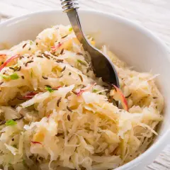 Schüssel mit Sauerkraut, verfeinert mit Kümmel und Apfelstücken. Eine Gabel ragt hinein, bereit zum Genießen.