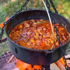 Herzhaftes Kesselgulasch-Rezept, das über offenem Feuer in einem Gusseisentopf köchelt. Fleischstücke, Kartoffeln und Paprika in einer würzigen Sauce.