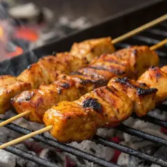 Saftige Schaschlik-Spieße brutzeln über glühender Kohle. Das Aroma von gegrilltem Fleisch steigt auf, während die Flammen im Hintergrund tanzen.