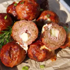 Leckere "Moink Balls" mit geschmolzenem Käse und Schinken im Inneren, glasiert und auf einem Blech mit Rosmarin garniert.