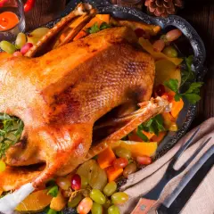 Goldbraun gebratene Gans auf einem festlichen Teller mit Früchten und Kräutern, bereit zum Servieren.