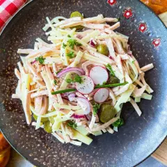 Ein herzhafter schweizer wurstsalat mit Käse, Radieschen, Gurken und Zwiebeln, garniert mit Petersilie.