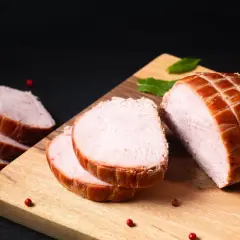 Ein aufgeschnittener Kassler-Braten mit perfekter Kerntemperatur, garniert mit Pfefferkörnern und Minze auf einem Holzbrett.