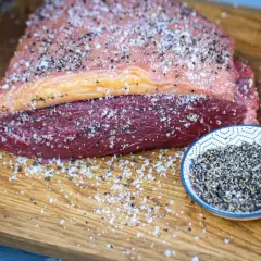 Ein roher Tafelspitz mit Salz und Pfeffer bestreut, bereit für das Tafelspitz grillen. Daneben eine Schale mit Pfefferkörnern.