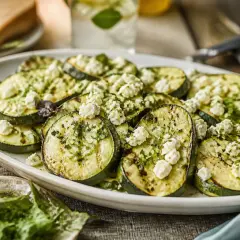 Gegrillte Zucchinischeiben mit zerbröseltem Feta und Kräutern, ein köstliches Gericht für den Sommer.