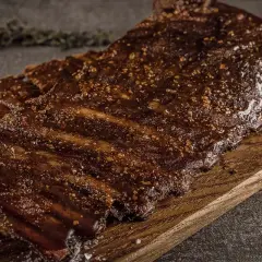 Saftige Rippchen vom Wildschwein, mariniert und perfekt gegrillt, liegen auf einem Holzbrett. Ein Genuss für jeden Grillmeister!