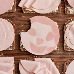 Biss in Lyoner: Welche Wurst ist gesund? Mehrere Brotscheiben mit Wurst belegt, liegen auf Holzuntergrund.
