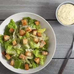 Frischer Caesar Salat mit knusprigen Croutons und Parmesan, dazu ein Schälchen cremiges Dressing.