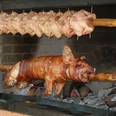 Ein Spanferkel grillen über offenem Feuer. Darüber hängen mehrere Hähnchen am Spieß.