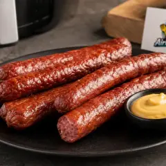 Leckere Cabanossi zubereiten: Fünf gebratene Würstchen auf einem Teller mit Senf. Perfekt für die Heißluftfritteuse.