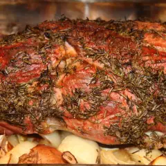 Saftige Lammkeule mit Rosmarin, bereit zum Grillen, liegt auf gerösteten Zwiebeln und Knoblauch.