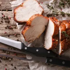 Saftiges braten fleisch, aufgeschnitten, mit Kräutern und Pfefferkörnern auf Holz. Messer und Fleischgabel liegen bereit.